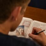 A person makes notes while reading a Bible with a photo of Jesus, focusing on study and faith.
